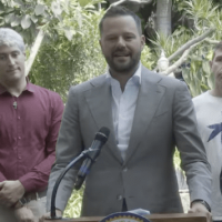 A man in a suit speaks at a podium outdoors, flanked by two men and two women, highlighting 2024 accomplishments. The podium displays a seal that reads "State Assembly," as lush greenery forms the backdrop, hinting at future plans for 2025 with Cal NORML's commitment to progress. CA Norml